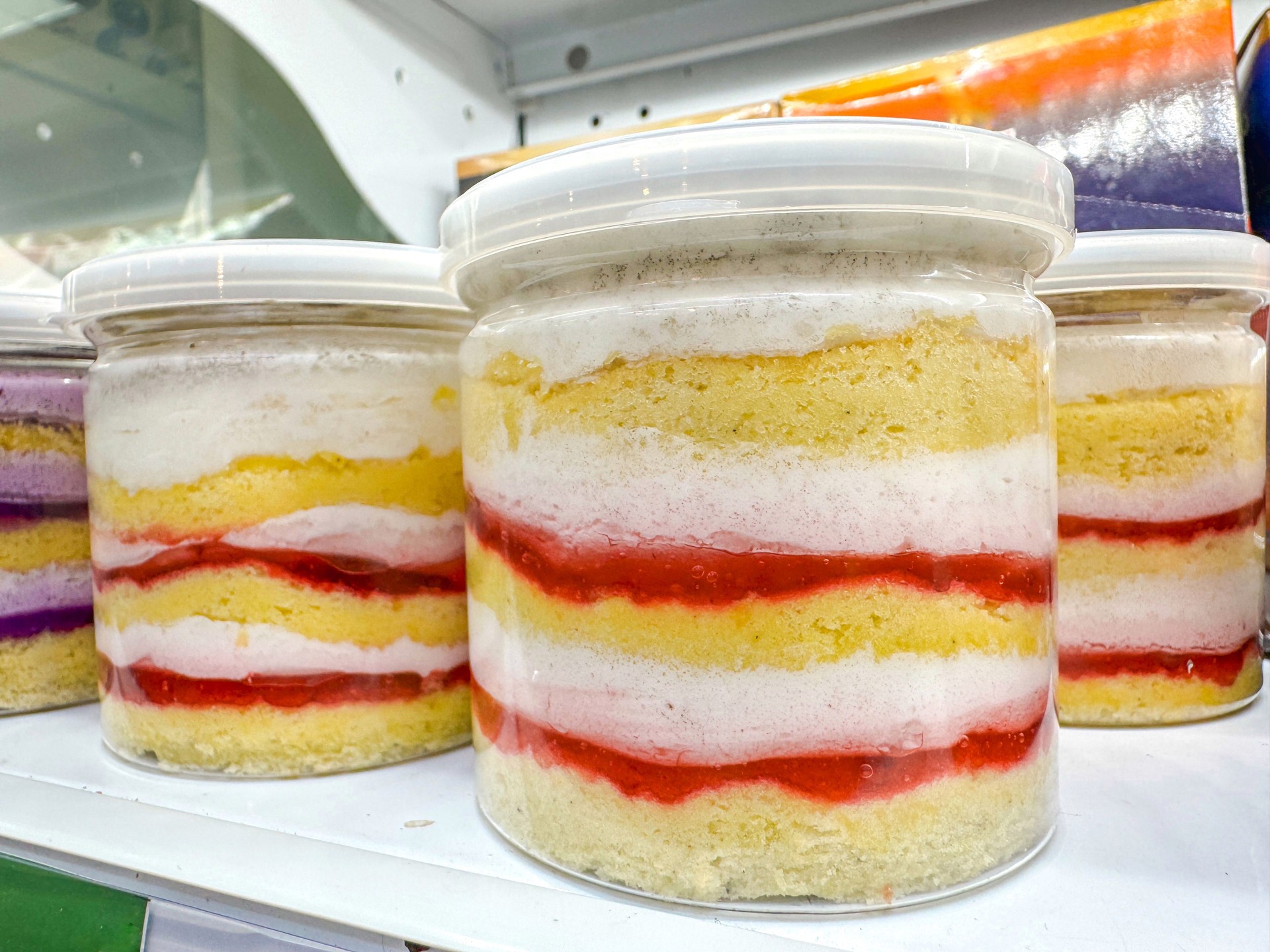 Strawberry cream layered cake in a jar on a minimart shelf. A visually appealing dessert featuring soft sponge cake alternated with pink strawberry cream, presented in a clear plastic jar with a lid.